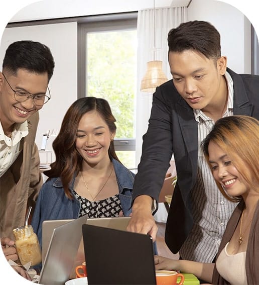 Four young professionals collaborating around laptops in a bright, modern workspace.